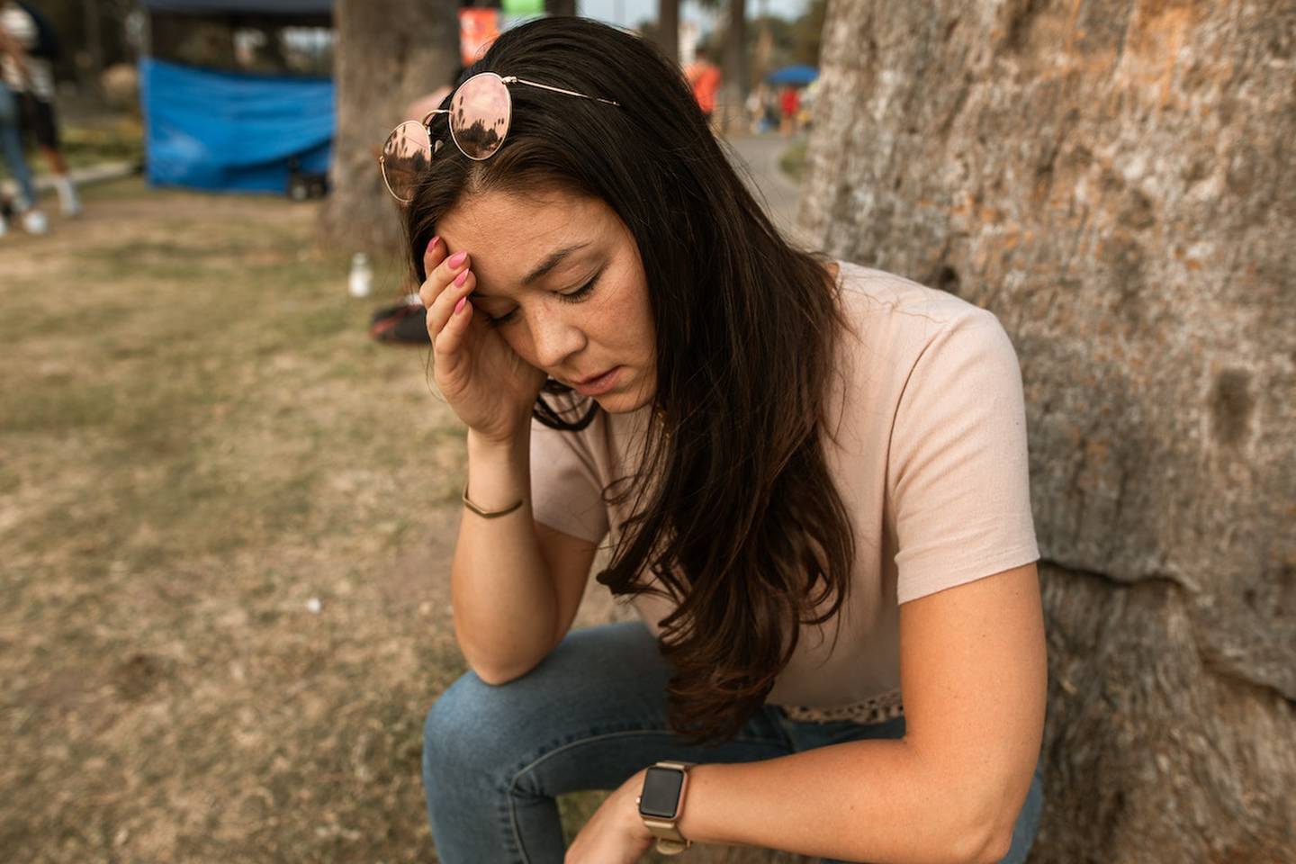 mujer sentada en un parque, tomándose la cabeza con una mano, en señal de agotamiento.