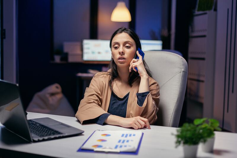 Mujer sentada en su oficina, con papeles de trabajo en la mesa y hablando por teléfono.