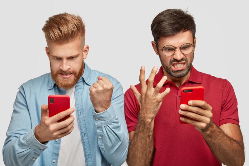 dos hombres mirando su celular y haciendo cara y gestos de enojados.