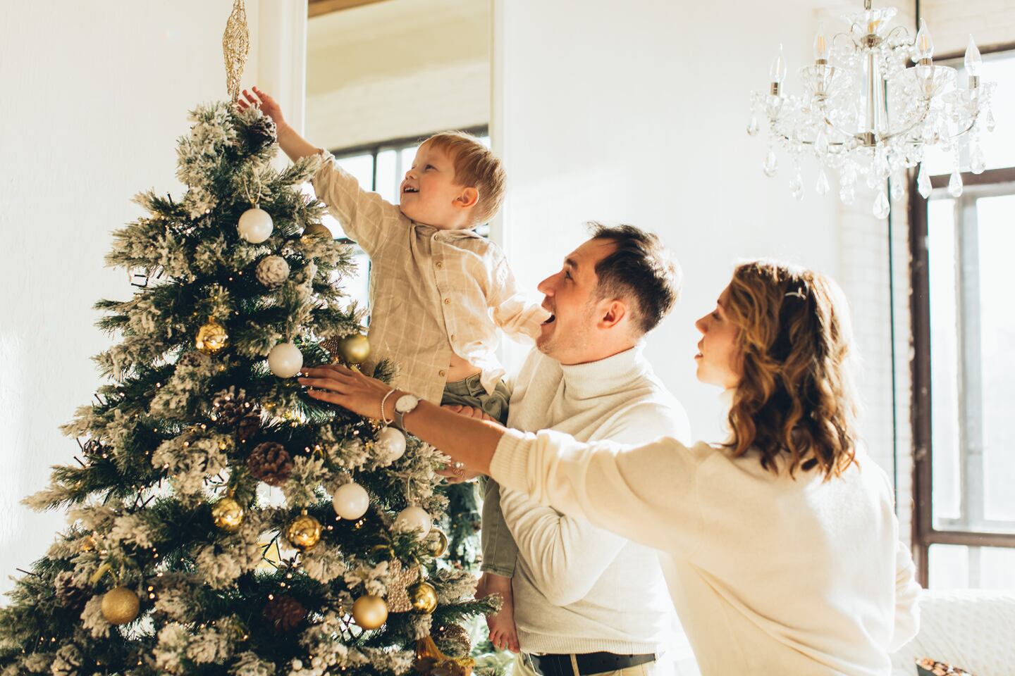 Familia decorando el árbol de Navidad mientras sonríen.