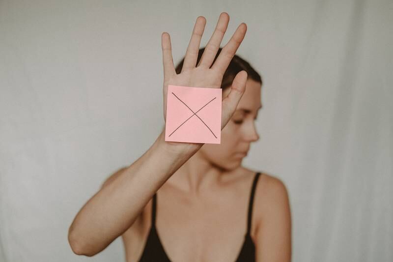 mujer mirando hacia el lado, con su mano hacia el frente, mostrando un post it con una X.