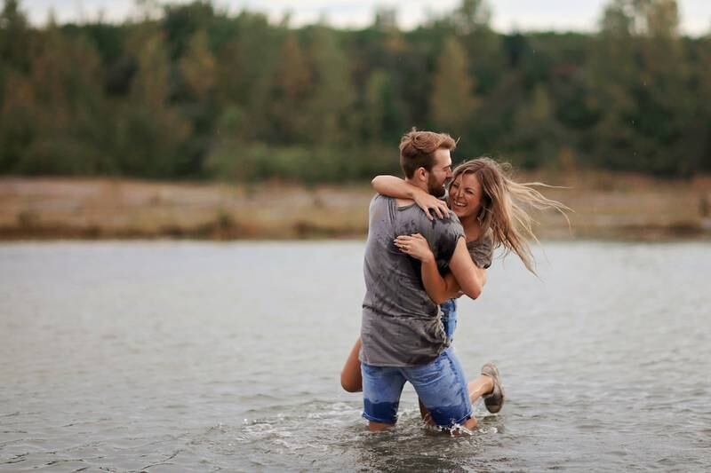 una pareja de un hombre y una mujer, riendo en un lago, mientras él la toma y la eleva.