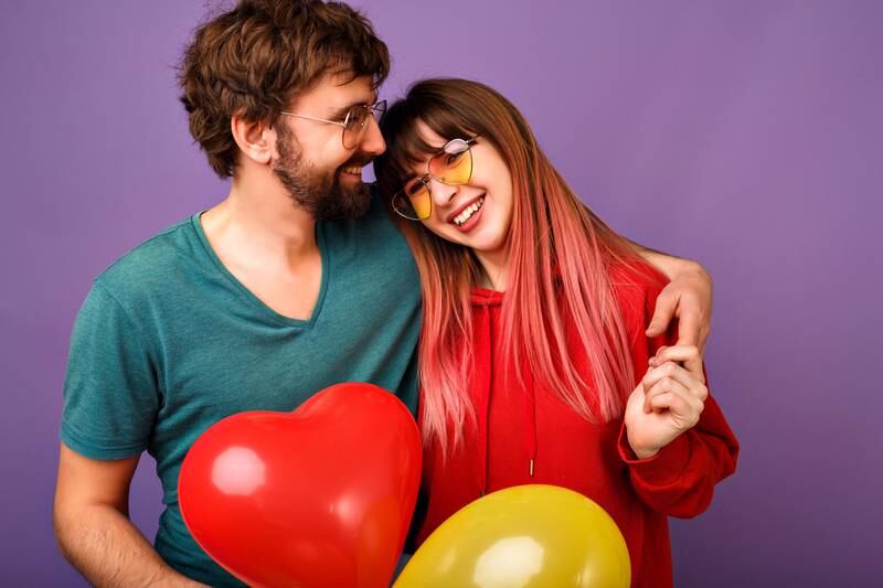Pareja de hombre y mujer se abrazan y sonríen mientras sostienen globos en forma de corazón.