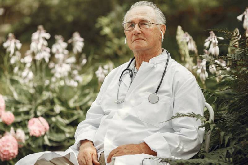 Médico jubilado portando un estetoscopio en el cuello, sentado en un jardín.