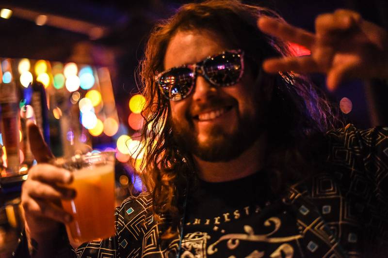 Hombre en una fiesta, con lentes de sol puestos y sosteniendo un vaso de bebida.