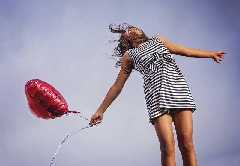 Mujer suspendida en el aire con expresión de felicidad y un globo con forma de corazón en su mano derecha.