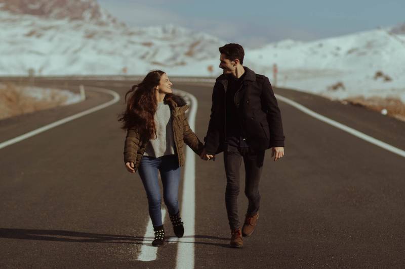 un hombre y una mujer tomados de la mano mientras se miran y caminan en medio de una carretera.
