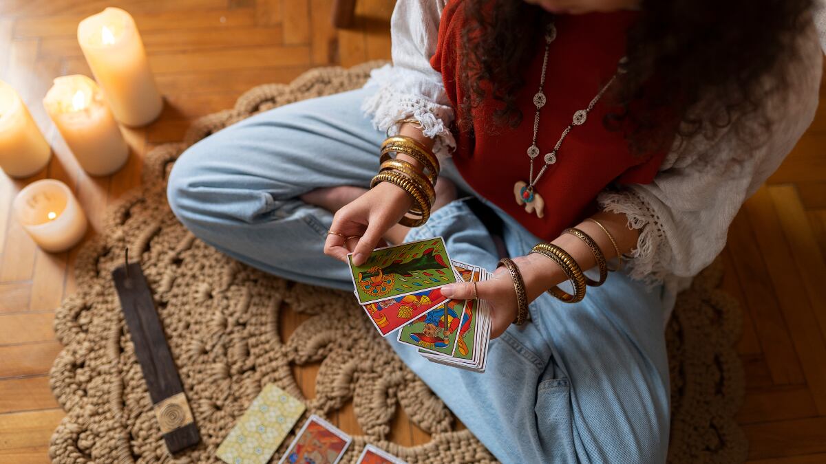 mujer sentada observando las cartas del Tarot que tiene en la mano.