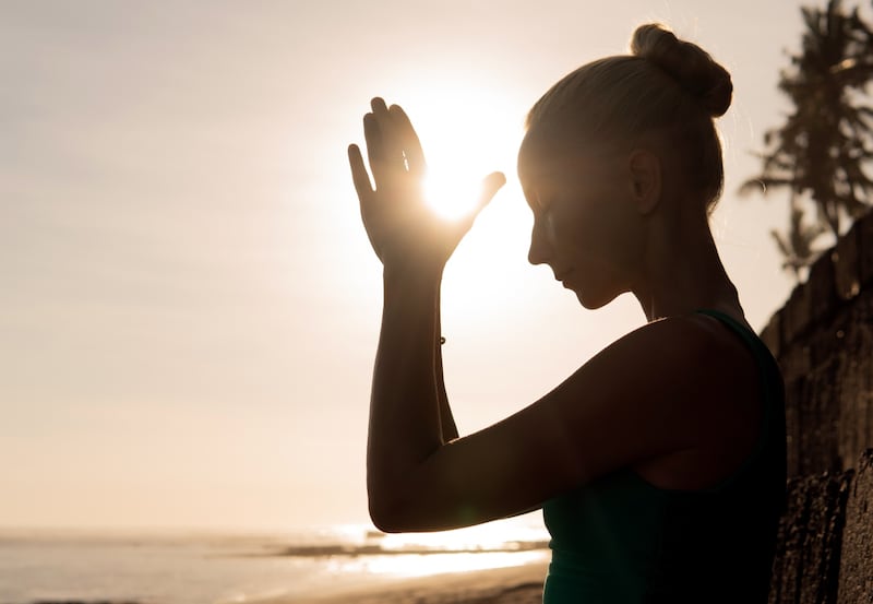 Mujer meditando a contraluz con el sol de fondo