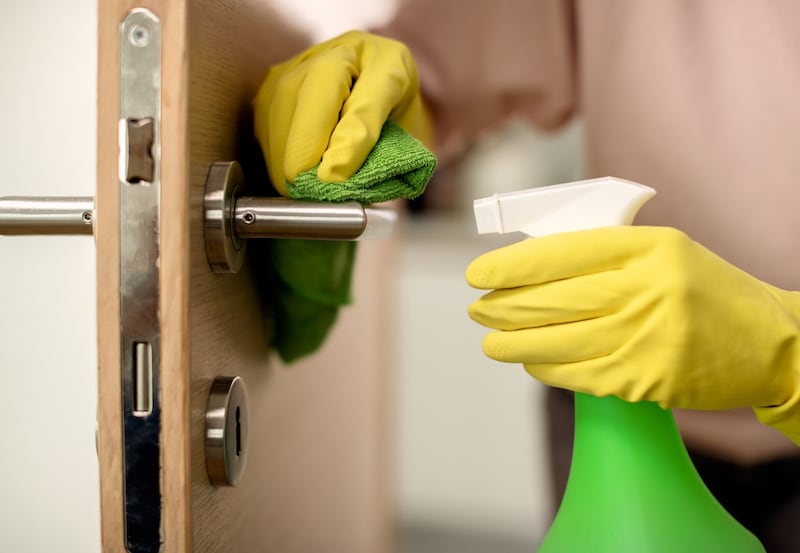 Manos enguantadas limpiando con un paño de microfibra el dintel y manilla de una puerta